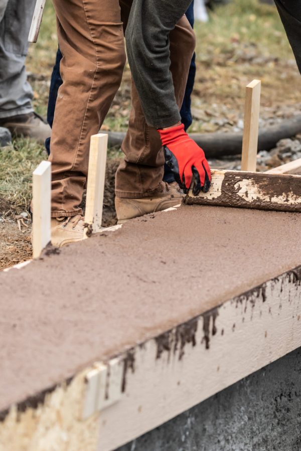 Construction Workers Pouring And Leveling Wet Cement Into Wood Framing.