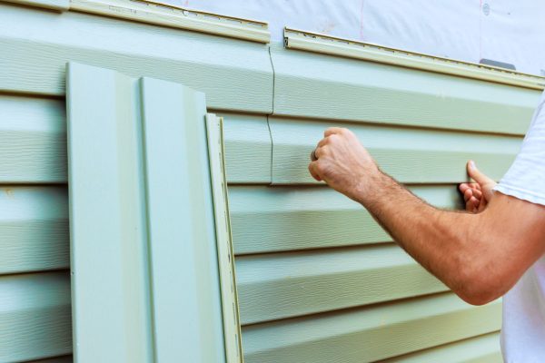 Worker carefully attaches green siding panels to house, focusing on precise fit for home renovation project.