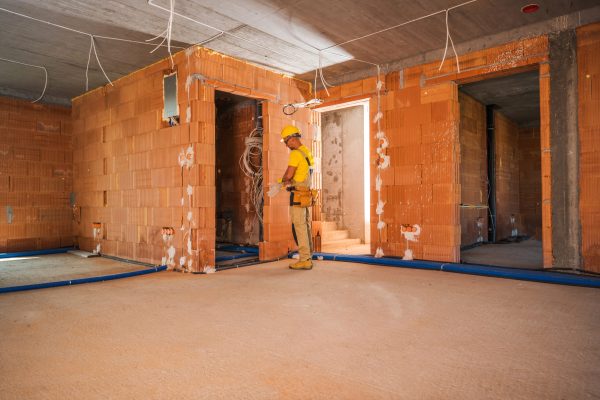 Newly Built Commercial Concrete Blocks Building. Caucasian Construction Worker in His 40s Wearing Head Safety Hard Hat and Gloves Finishing Building Interior Industrial Theme.