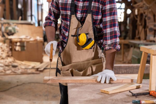Carpenters analyzing construction blueprint together in a woodworking shop, surrounded by tools and wooden materials on the workbench.