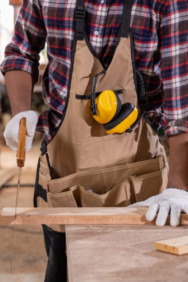 Carpenters analyzing construction blueprint together in a woodworking shop, surrounded by tools and wooden materials on the workbench.