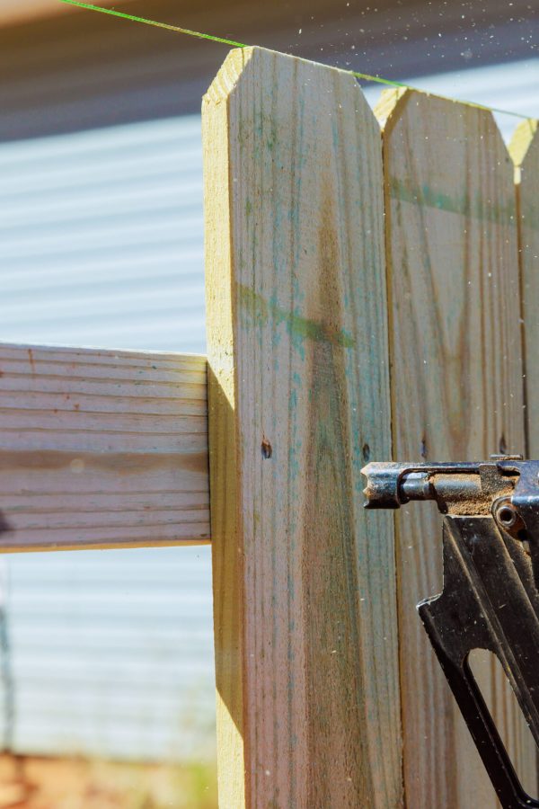Nailer using air pneumatic gun to secure wooden plank fence during work