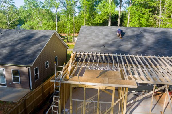 Carpenter hammering nails into OSB plywood panels on roof of construction site