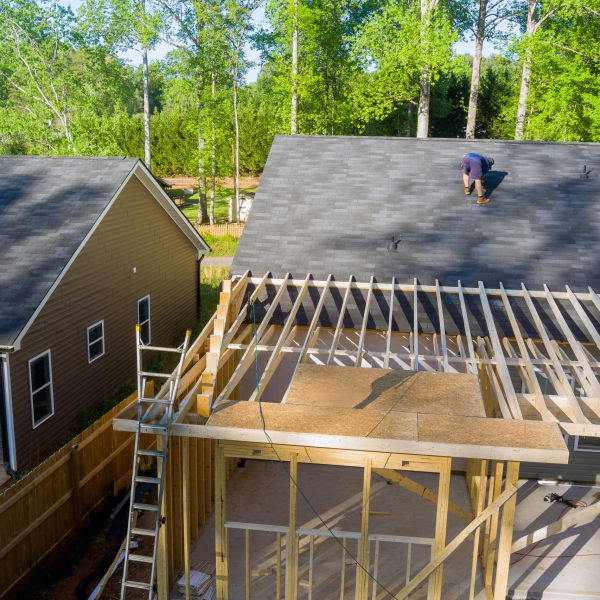 Carpenter hammering nails into OSB plywood panels on roof of construction site