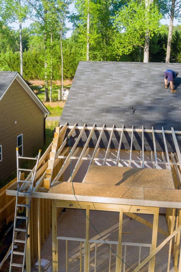 Carpenter hammering nails into OSB plywood panels on roof of construction site