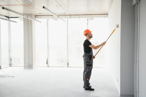 The man is painting the wall. DIY repair. The painter holds the roller near the wall.