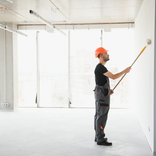 The man is painting the wall. DIY repair. The painter holds the roller near the wall.